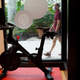 A Peloton bike sitting on a store's showroom floor while people walk by outside the store window.